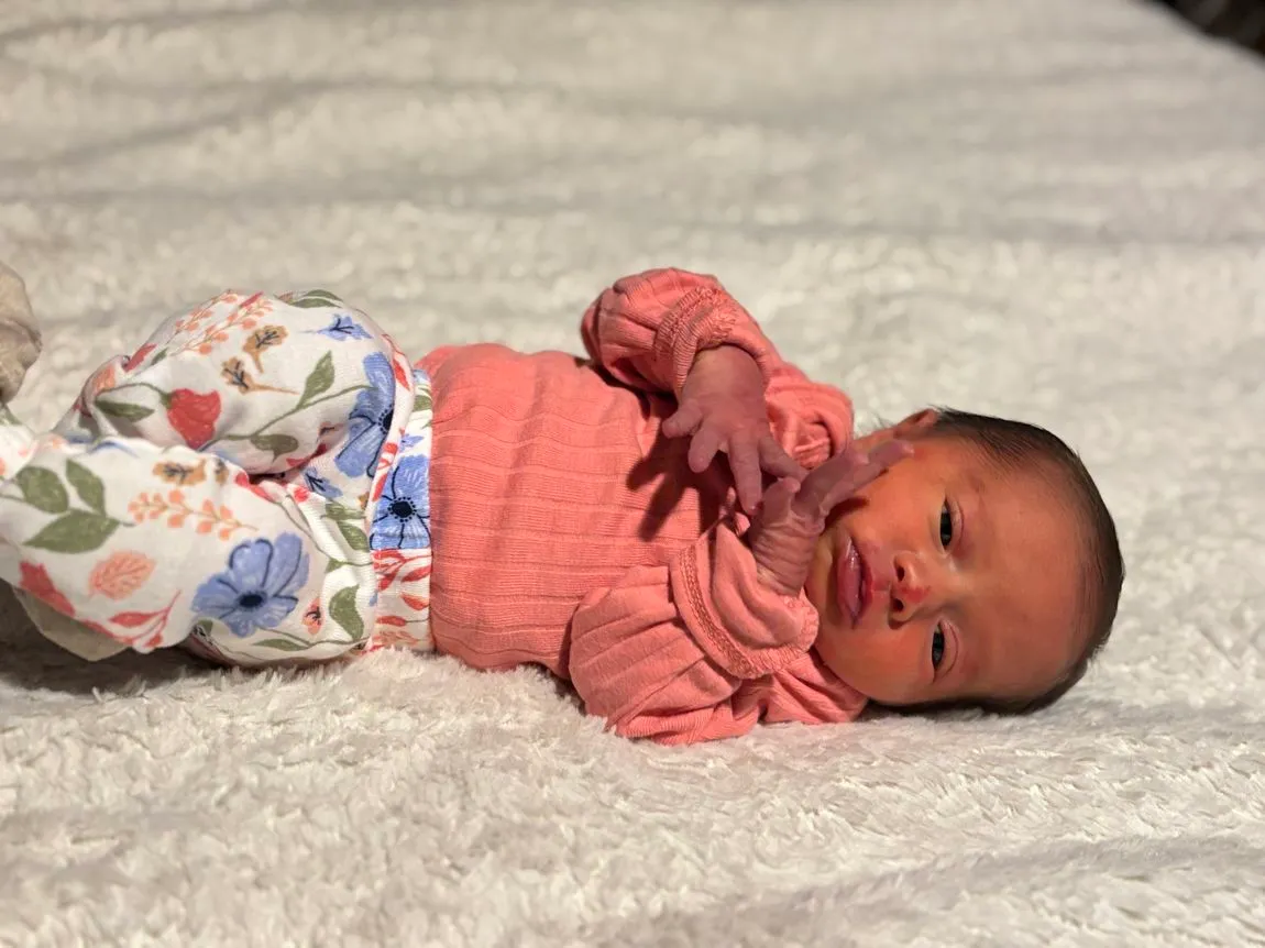 Baby in pink shirt and floral pants laying down