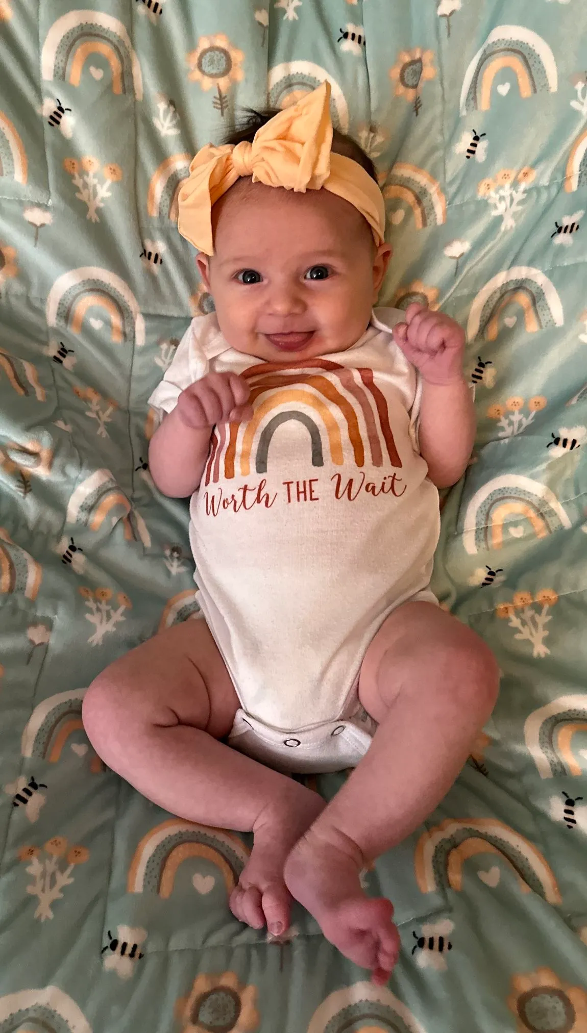 Smiling baby in a rainbow onsie on a rainbow blanket