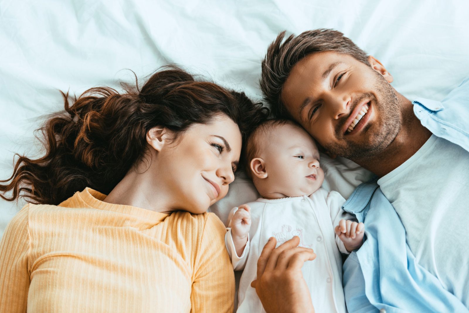 Happy husband and wife lying on bedding near baby